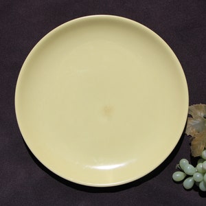 May include: A pale yellow ceramic dinner plate with a slightly rough texture. The plate is on a dark brown surface.