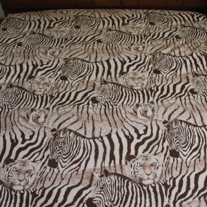 Puede incluir: Una s&aacute;bana con un patr&oacute;n repetitivo de cebras y tigres en color marr&oacute;n y blanco. El dise&ntilde;o muestra m&uacute;ltiples cabezas y cuerpos de animales dispuestos sobre la superficie de la tela, creando un efecto visual denso y superpuesto con rayas.