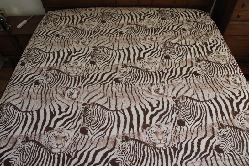 Puede incluir: Una s&aacute;bana con un patr&oacute;n repetitivo de cebras y tigres en color marr&oacute;n y blanco. El dise&ntilde;o muestra m&uacute;ltiples cabezas y cuerpos de animales dispuestos sobre la superficie de la tela, creando un efecto visual denso y superpuesto con rayas.