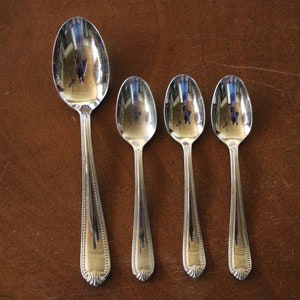 May include: Four silver spoons of varying sizes, arranged in a row from largest to smallest on a brown wooden surface.