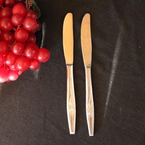 May include: Two silver dinner knives with ornate designs on the handles.