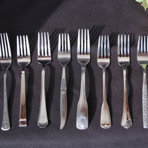 May include: Eight silver forks with different designs on a black background. The forks are arranged in a row from left to right.