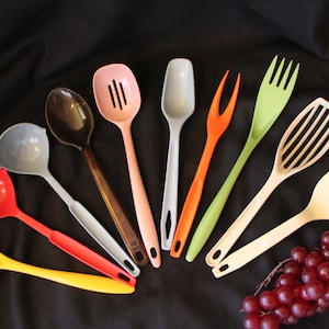 May include: A collection of colorful kitchen utensils, including ladles, spoons, forks, and a spatula, arranged on a dark background. The utensils are in various colors such as red, yellow, brown, pink, and green, suggesting a vibrant and functional kitchen set.