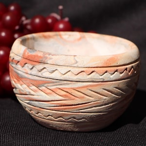 Puede incluir: Un cuenco de cerámica hecho a mano con superficie texturizada y patrones geométricos tallados. El cuenco presenta una paleta de colores beige, naranja y gris. Una pieza decorativa para el hogar.