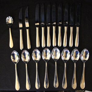 May include: A set of 15 silver-toned utensils, including 12 knives and 3 spoons. The utensils are arranged in a row on a black surface.