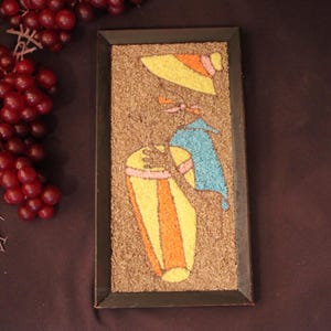 May include: A rectangular wall art piece featuring a textured cork background with a mosaic-style design made of colored granules. The image depicts a figure wearing a yellow hat and blue top, playing a tall, orange and yellow striped drum.