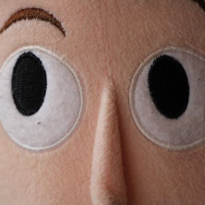 Puede incluir: Primer plano de la cara de un juguete de peluche con dos ojos grandes y blancos con pupilas negras. El juguete tiene una ceja marr&oacute;n y una nariz larga y rosada.