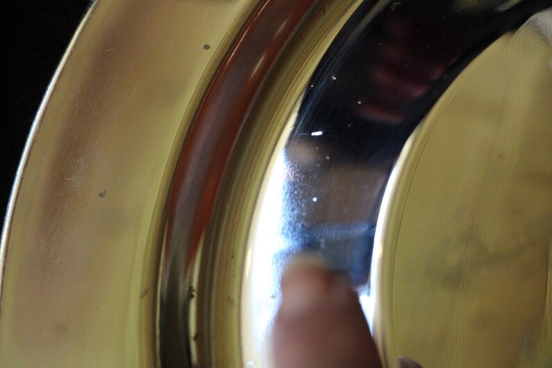 Puede incluir: Primer plano de una secci&oacute;n de un plato o cuenco de color dorado, posiblemente de lat&oacute;n. La superficie es reflectante, con una banda roja oscura y un reflejo oscuro. La imagen est&aacute; bien iluminada, mostrando los detalles del metal.