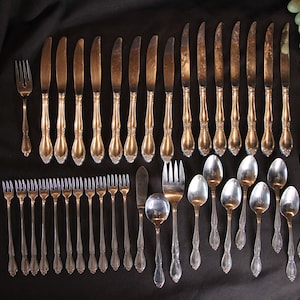 May include: A set of silver cutlery, including knives, forks, and spoons, arranged on a black surface. The cutlery is polished and shiny, with ornate handles.