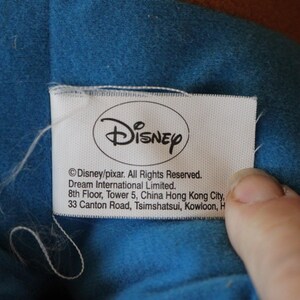 Puede incluir: Una etiqueta blanca con el logotipo de Disney y el texto "Disney/pixar. Todos los derechos reservados. Dream International Limited. 8&ordm; piso, Torre 5, China Hong Kong City, 33 Canton Road, Tsimshatsui, Kowloon, H"