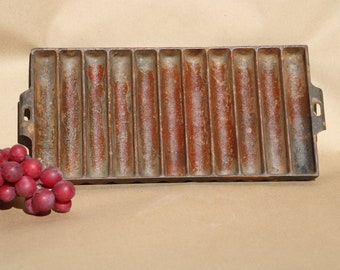 May include: Vintage cast iron baking pan with 12 individual molds. The pan is rusty brown and has a rectangular shape.