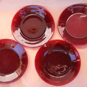 May include: Four red glass plates with a raised rim and a slightly textured surface. The plates are all the same size and shape.