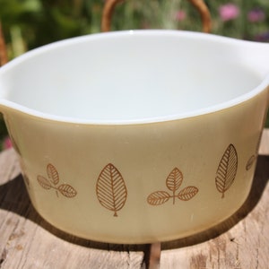 May include: A vintage yellow mixing bowl with a gold leaf design. The bowl is made of Pyrex glass and has a smooth, glossy finish.