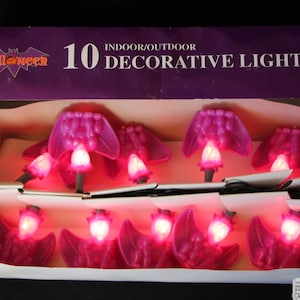 May include: A set of 10 indoor/outdoor decorative lights featuring a bat design. The lights are pink and have a glowing red bulb in the center. The box says "Halloween" and "10 Decorative Light Set".