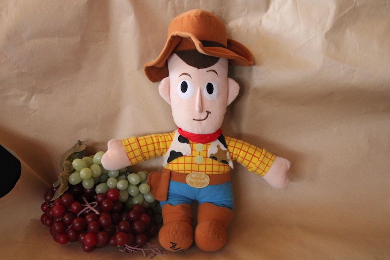 Puede incluir: Un juguete de peluche de Woody de Toy Story. Lleva su caracter&iacute;stico sombrero de vaquero marr&oacute;n, camisa amarilla y azul y botas marrones. Tiene una sonrisa amigable y sostiene una bandana roja.