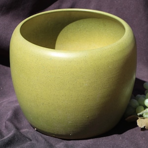 May include: A large, round, green ceramic planter with a speckled finish. The planter is sitting on a dark brown fabric surface.