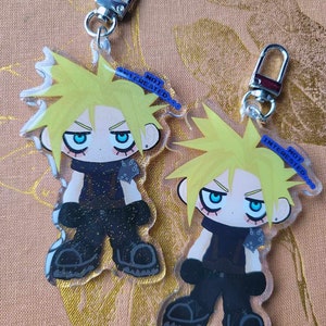 Może przedstawiać: Dwa przezroczyste akrylowe breloki do kluczy przedstawiające postać z kreskówki z kolczastymi żółtymi włosami, niebieskimi oczami i czarnymi ubraniami. Każdy brelok ma srebrne zapięcie i niebieski baner z napisem "NOT INTERESTED".