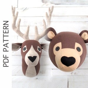 Pode incluir: Uma decoração de parede de cabeça de veado e urso marrom feita de feltro. O veado tem grandes chifres e o urso tem um nariz preto e olhos pretos.