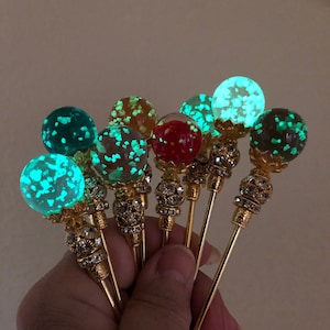 May include: A collection of seven decorative pins featuring spherical tops filled with glowing, multi-coloured flecks. Each pin has a gold-toned metal shaft, a filigree base, and a band of small, clear crystals set into the metal below the sphere.