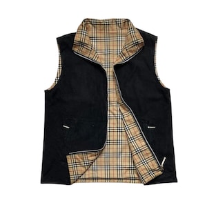 Op de afbeelding: Omkeerbaar zwart vest met een volledige ritssluiting. De binnenvoering en kraag hebben een klassiek ruitpatroon in bruin, rood en zwart. Het vest heeft twee kleine zakken en een hoge kraag.