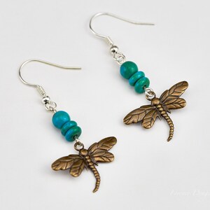 Op de afbeelding: Een paar zilveren oorhangers met turquoise kralen en bronzen libellenbedels.