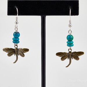 Op de afbeelding: Turquoise en bronzen libellen oorbellen met zilveren haakjes. De libel charme is gedetailleerd met een textuur.