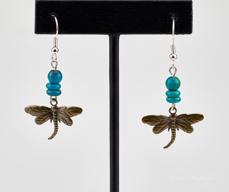 Op de afbeelding: Turquoise en bronzen libellen oorbellen met zilveren haakjes. De libel charme is gedetailleerd met een textuur.