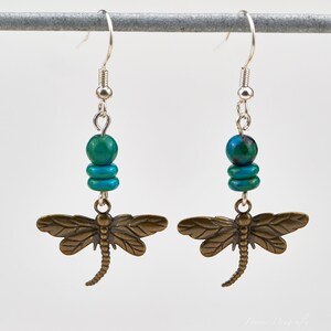 Op de afbeelding: Een paar oorhangers met een bronzen libellenbedel en turquoise kralen. De oorbellen hebben zilveren haakjes.