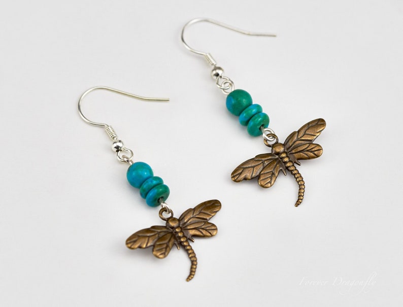 Op de afbeelding: Een paar zilveren oorhangers met turquoise kralen en bronzen libellenbedels.
