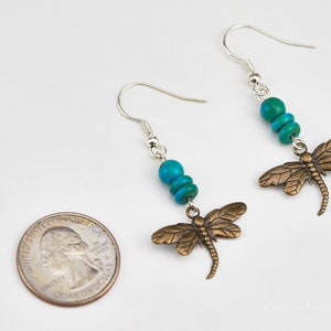Op de afbeelding: Een paar zilveren oorhangers met turquoise kralen en bronzen libellenbedels. De oorhangers zijn ongeveer zo groot als een Amerikaanse kwart.
