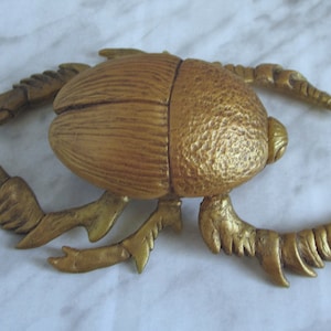 May include: A gold-coloured scarab beetle figurine with detailed legs and a textured body.