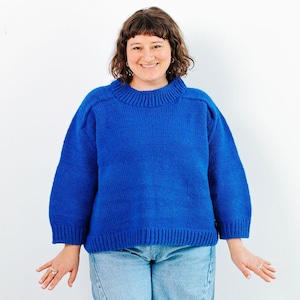 May include: A vibrant blue sweater with a ribbed crew neck and long sleeves. The sweater is made of a soft, knitted material. The model is wearing light blue jeans. The background is plain white.