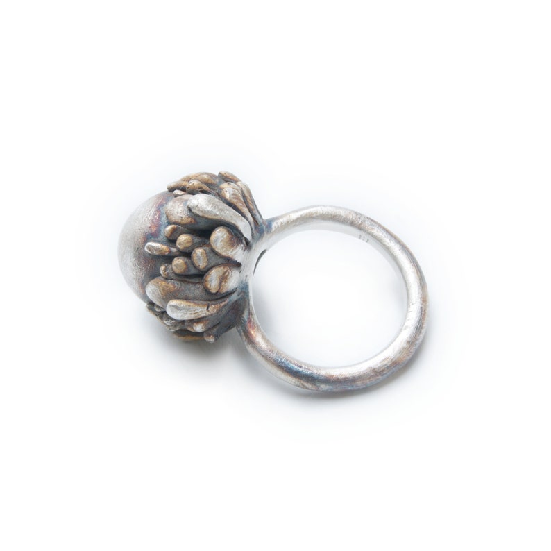 May include: A silver ring with a textured, organic-shaped design. The ring is made of metal and has a silver finish.