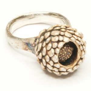 May include: A silver ring with a textured, round, flower-like design. The center of the flower is a smaller, round, textured piece.