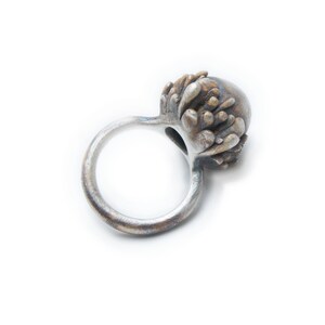 May include: A silver ring with a textured, organic-shaped top. The top is a dark silver color with a hint of gold.