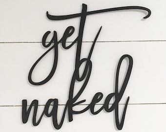 May include: Black wooden sign with the words "get naked" in a cursive font. The sign is mounted on a white, horizontal-slat background, creating a contrast between the dark text and the light backdrop. The sign is suitable for a bathroom.
