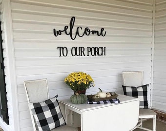 May include: A white porch setting with a drop-leaf table, two chairs, and decorative pillows. The table is adorned with a fall arrangement, pumpkins, and a black and white checkered runner. The words "welcome TO OUR PORCH" are displayed on the wall.