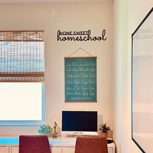K&ouml;nnte beinhalten: Ein Heimb&uuml;ro mit einem wei&szlig;en Schreibtisch, Computer und einer t&uuml;rkisfarbenen Alphabettabelle. An der Wand befindet sich ein schwarzes Metallschild mit der Aufschrift "HOME SWEET homeschool". Ein Fenster mit Bambusjalousie ist ebenfalls zu sehen.