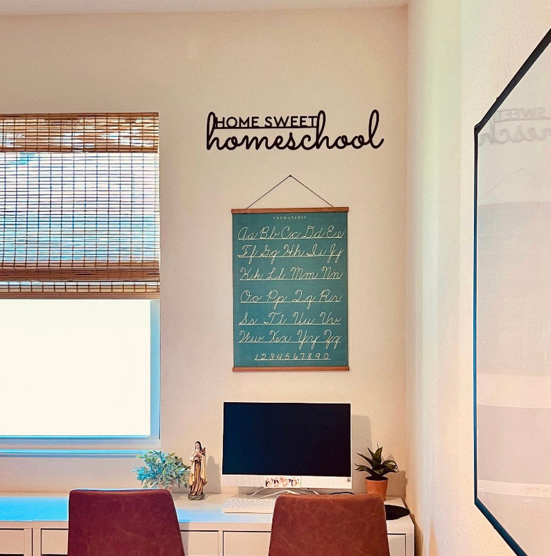 K&ouml;nnte beinhalten: Ein Heimb&uuml;ro mit einem wei&szlig;en Schreibtisch, Computer und einer t&uuml;rkisfarbenen Alphabettabelle. An der Wand befindet sich ein schwarzes Metallschild mit der Aufschrift "HOME SWEET homeschool". Ein Fenster mit Bambusjalousie ist ebenfalls zu sehen.