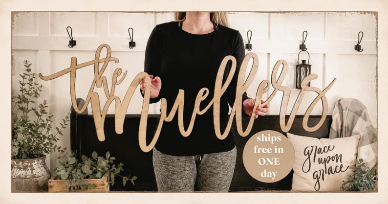 May include: A wooden sign that reads "the Muellers" in a cursive font. The sign is held in front of a white wall with black hooks and a black bench. A pillow with the words "grace upon grace" is visible.