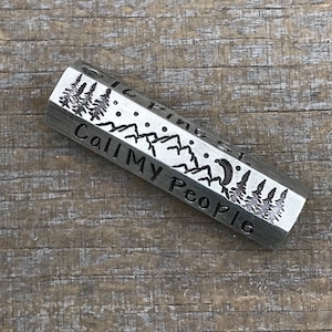 May include: A silver hexagonal keychain with an engraved design of mountains, trees, a crescent moon, and stars. The text "Call My People" is engraved on the keychain.