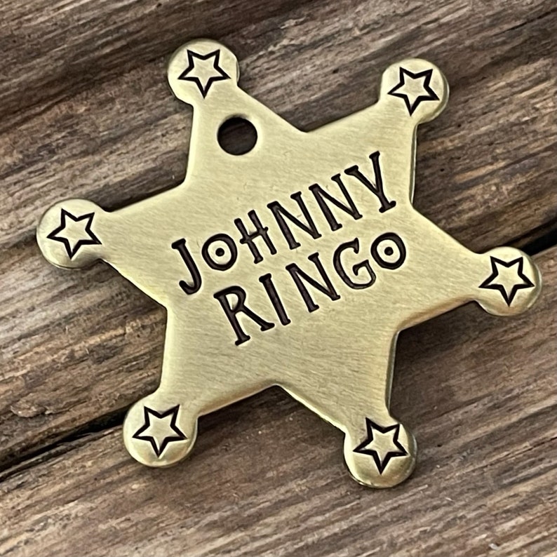 Peut inclure: Une &eacute;toile de sh&eacute;rif en m&eacute;tal dor&eacute; &agrave; cinq branches, avec le texte grav&eacute; "JOHNNY RINGO".