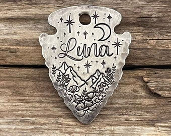 May include: A silver arrowhead charm with an engraved design of mountains, stars, a crescent moon, and the word "Luna".