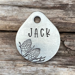 May include: Silver dog tag with a pine cone design and the name "JACK" engraved on it.