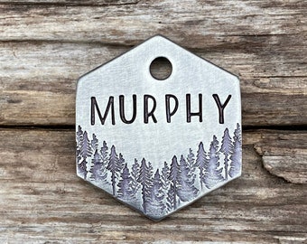 May include: Silver hexagonal dog tag with a forest silhouette design and the name "MURPHY" engraved in black.