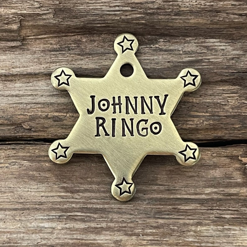 Peut inclure: Un badge en forme d'&eacute;toile de sh&eacute;rif de couleur dor&eacute;e avec le texte "JOHNNY RINGO" grav&eacute; dessus.