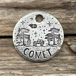 Op de afbeelding: Ronde zilveren hondenpenning met een zwart-wit ontwerp van een auto die door een besneeuwd bos rijdt met sterren en een komeet aan de hemel. De tekst "COMET" is gegraveerd op de penning.