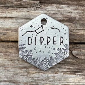 May include: A silver hexagonal tag with a constellation design and the word "DIPPER" engraved on it. The tag is surrounded by a fern leaf design.