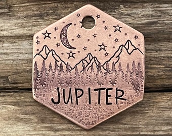 May include: Copper hexagon-shaped pet tag with a mountain range, crescent moon, and stars design. The text "JUPITER" is engraved on the tag.