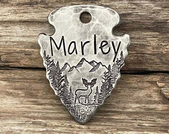 May include: Silver arrowhead-shaped pet tag with a deer silhouette, mountain range, and pine trees engraved on it. The tag is personalized with the name "Marley".